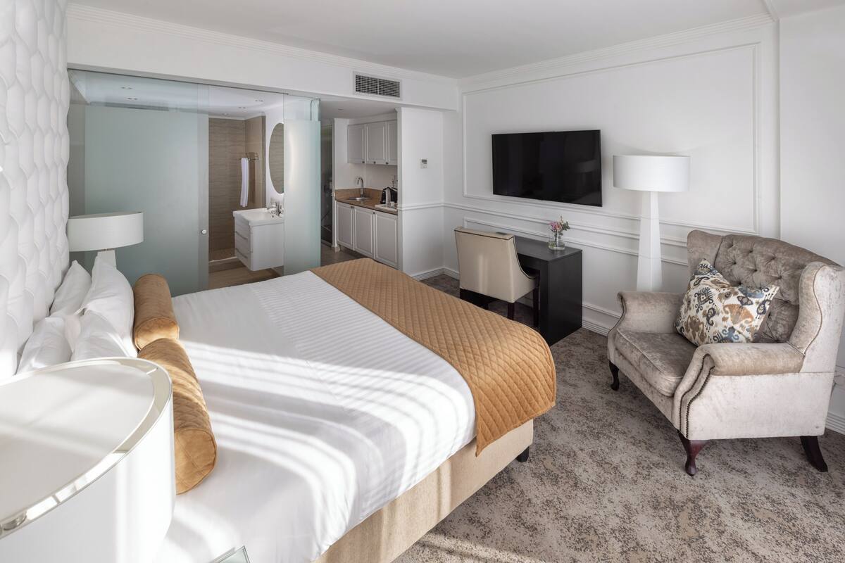 Habitación de hotel con una cama grande, un escritorio, una silla, un televisor y un baño con espejo y lavabo.