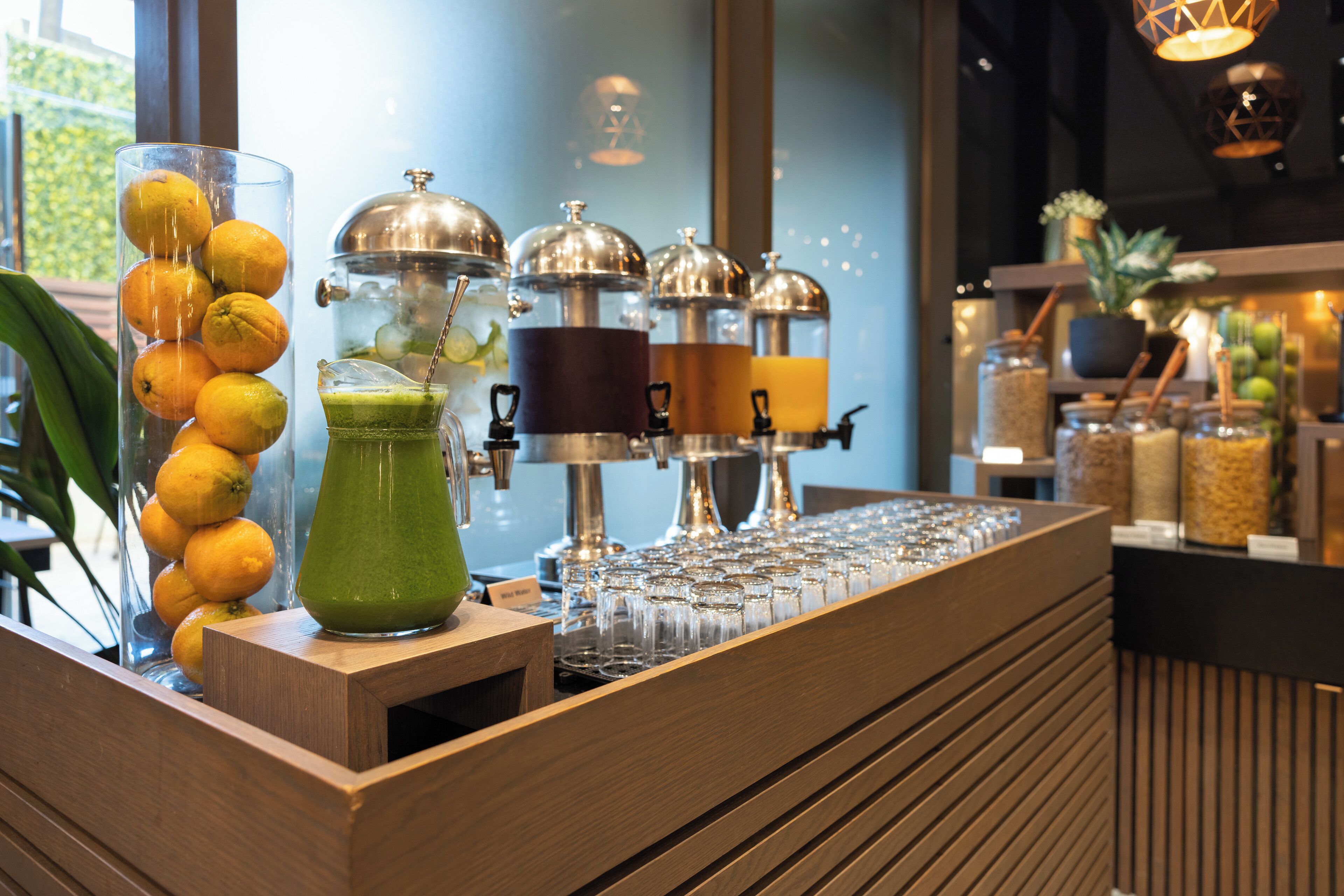 A bar area with a wooden counter, a glass container with lemons, a green drink, and a coffee machine.