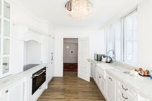 A bright kitchen with white cabinetry, a marble countertop, a chandelier, and a wooden floor.