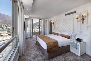A hotel room with a large bed, a nightstand, and a view of the city.