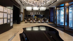A modern hotel lobby with a large chandelier, a reception desk, framed certificates on the wall, and a seating area with tables and chairs.