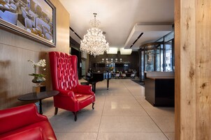 A modern lobby with a red leather chair, a grand chandelier, and a piano.