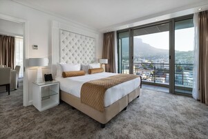 A modern hotel room with a large bed, a glass-enclosed balcony, and a city view.