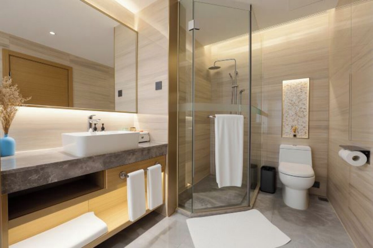Un baño moderno con ducha envuelta en vidrio, un espejo grande, un lavabo blanco y un inodoro.