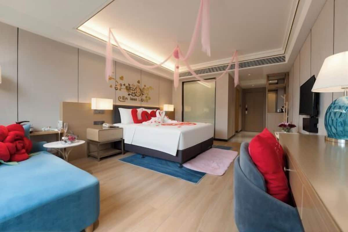 A modern hotel room with a bed, a desk, a chair, a TV, and a wall with decorative elements.