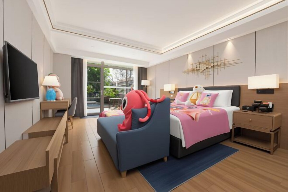 Una habitación de hotel moderna con una cama, un escritorio, una silla, un televisor y un ventanal grande.