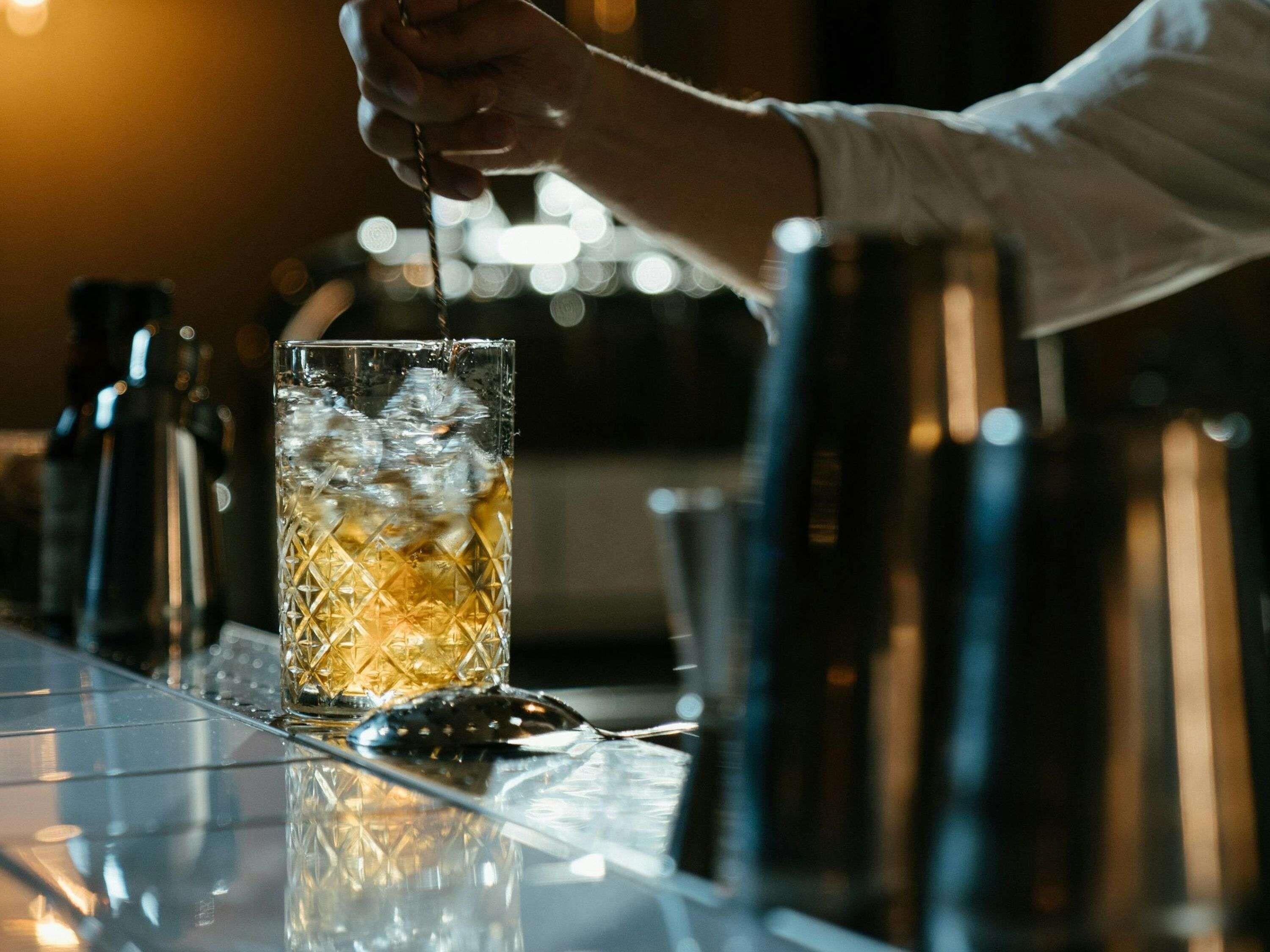 A bartender pouring a drink into a glass with ice.