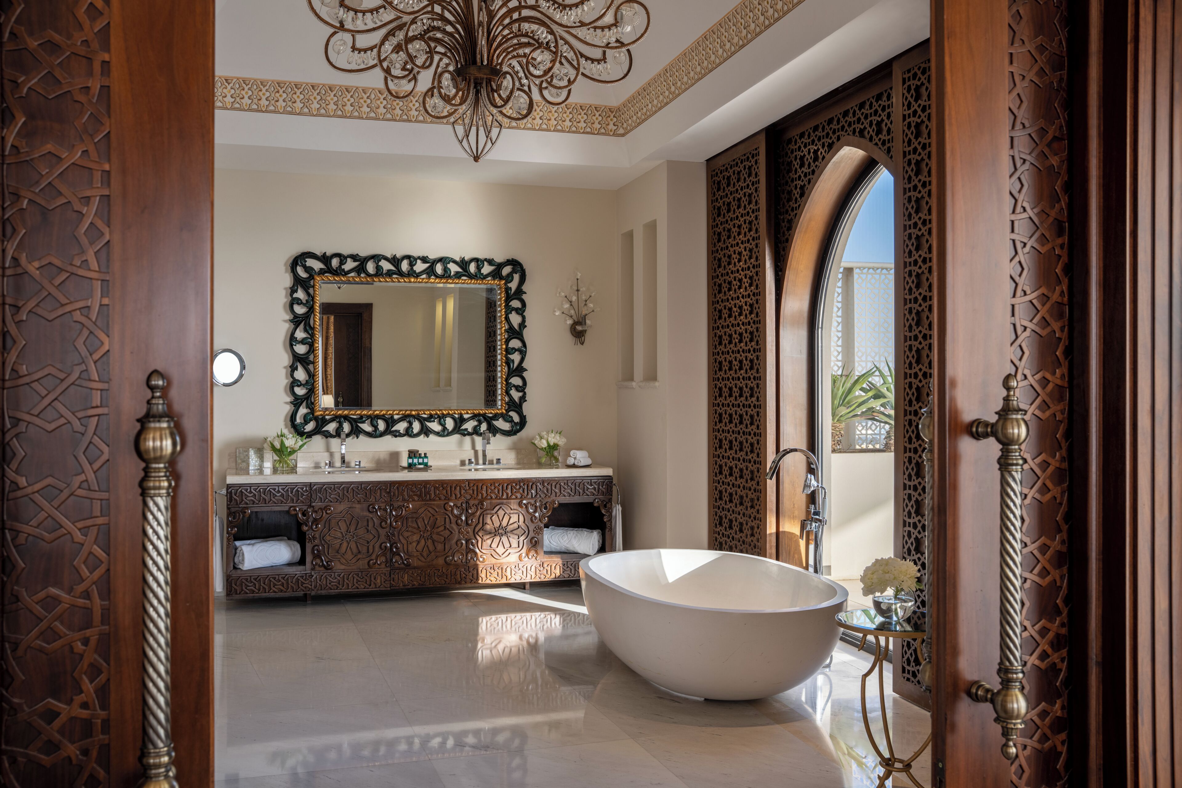 Un baño lujoso con una bañera independiente, un espejo ornamentado y elaborados diseños en la pared.