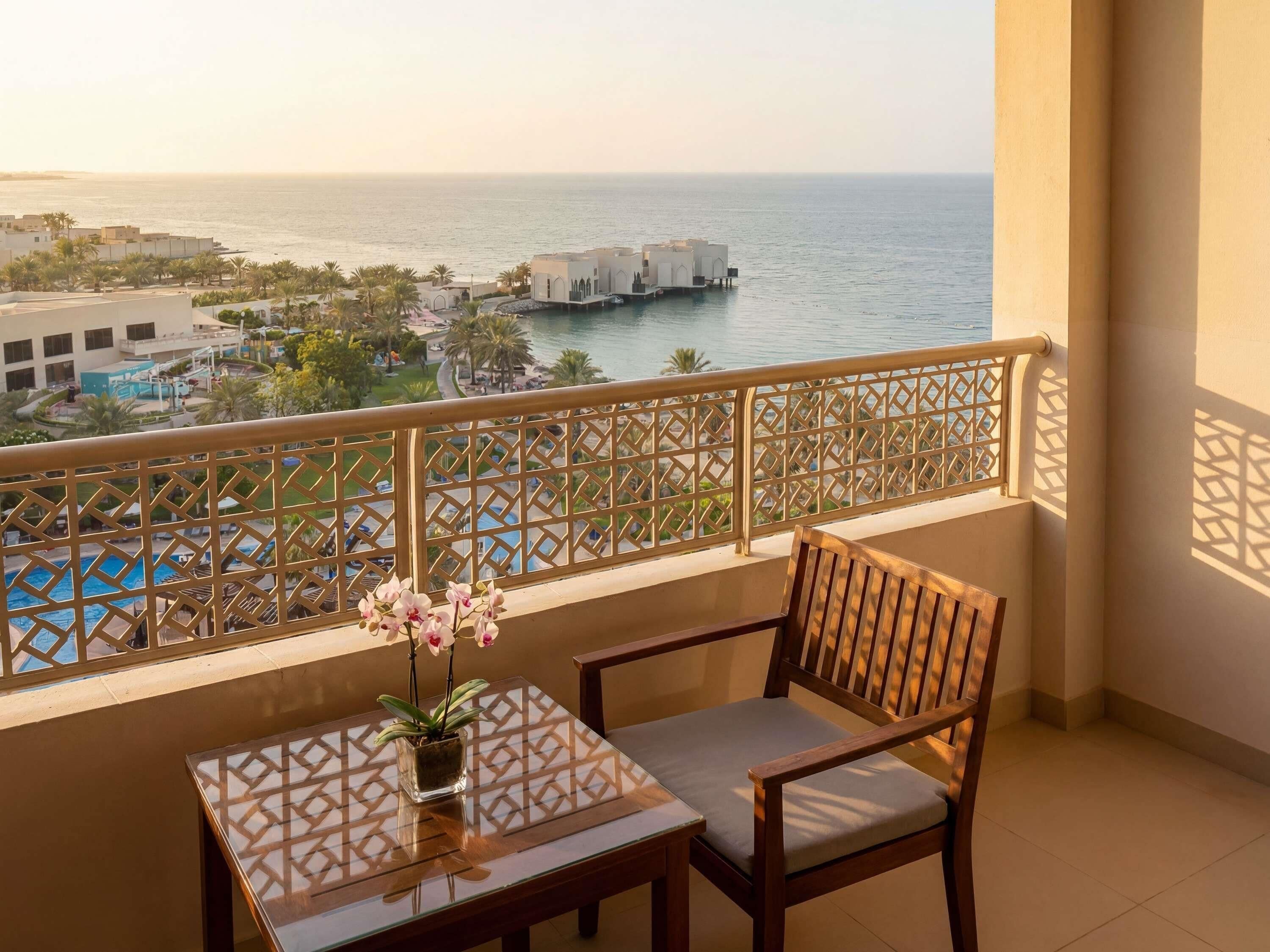 A balcony with a view of the sea, a pool, and a building with a white facade.