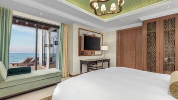 A hotel room with a large bed, a desk, a TV, and a view of the sea.