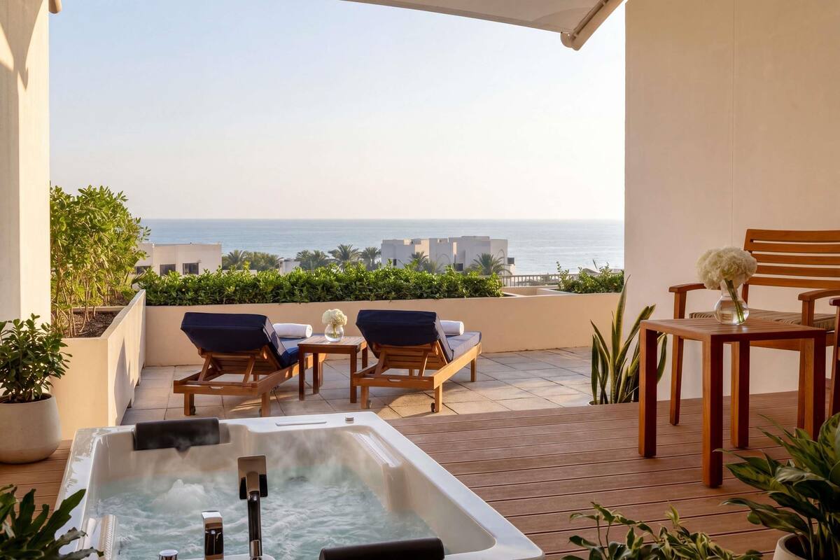A balcony with a hot tub, lounge chairs, and a table with a vase of flowers.