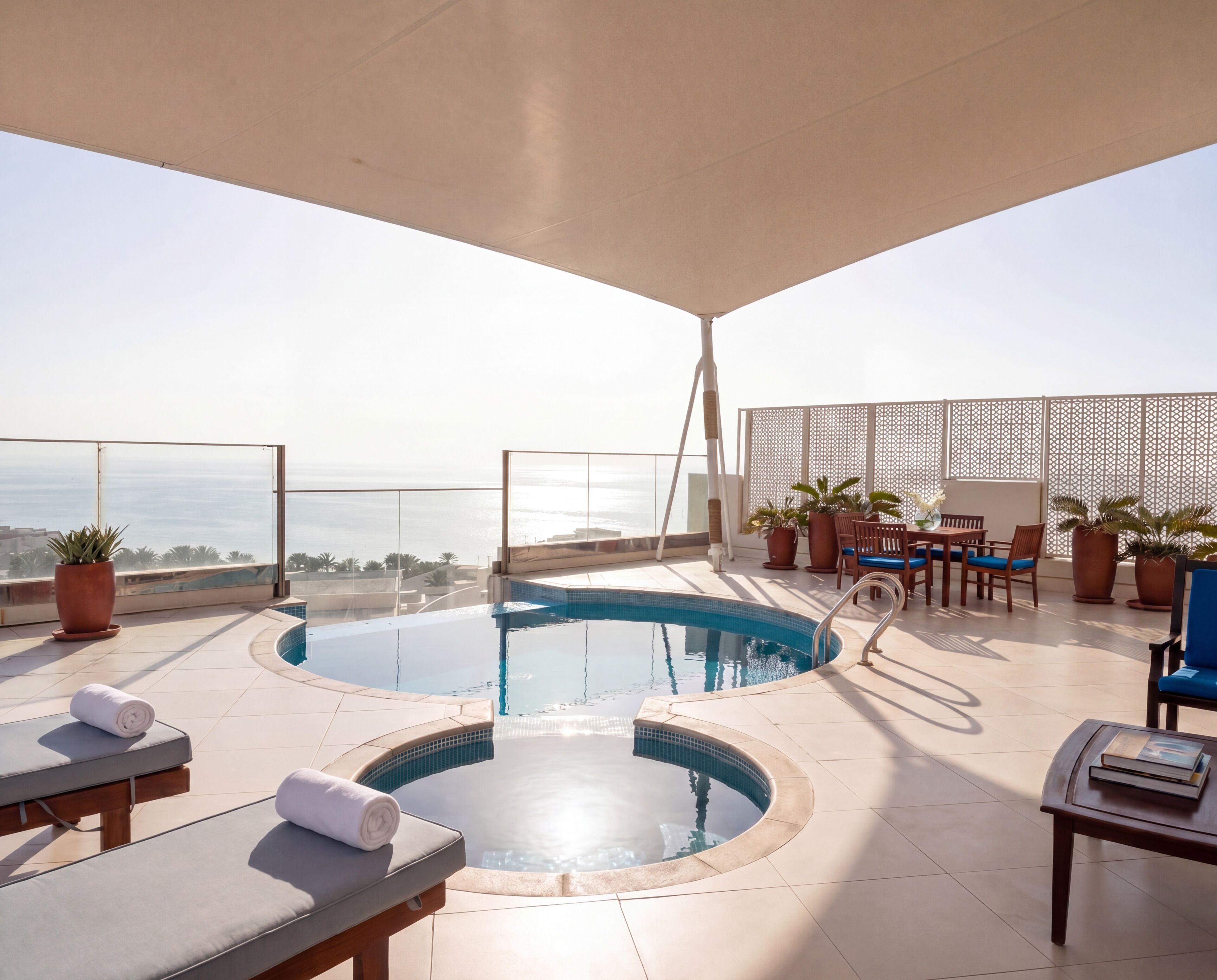 Una piscina infinita en la azotea con sillones de descanso y una mesa, rodeada de plantas en macetas y vistas al océano.