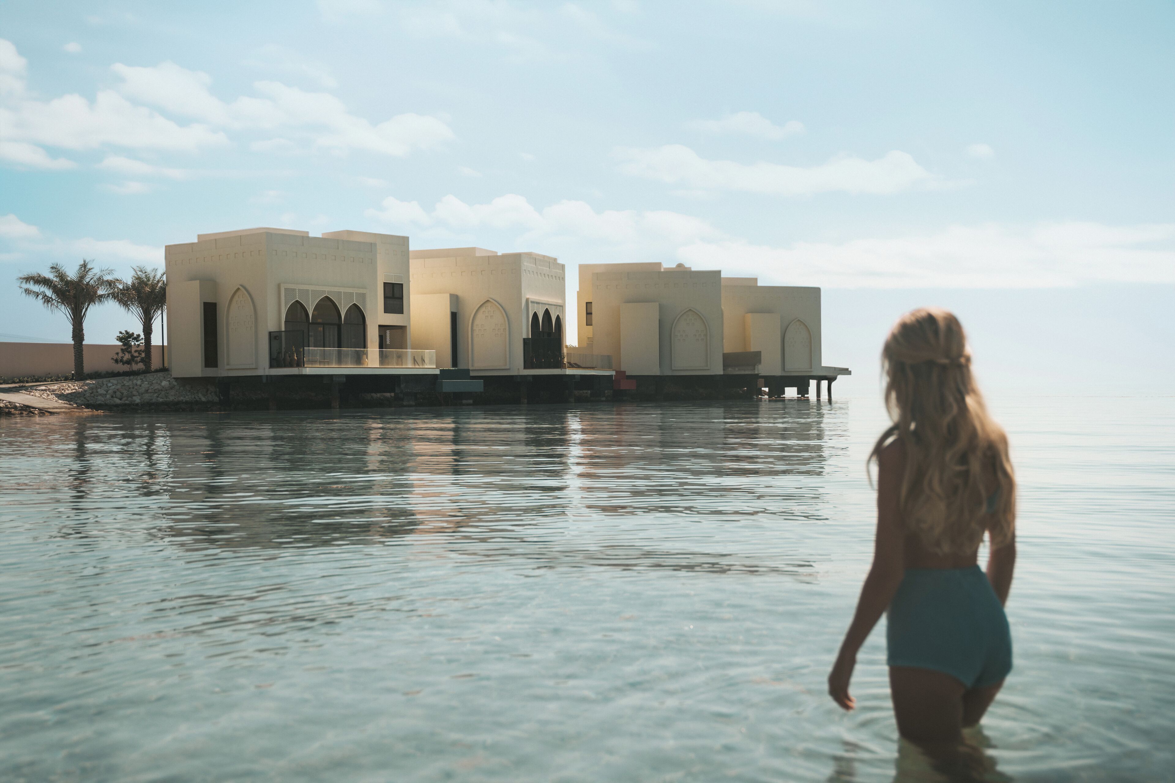 A modern building with arched windows and a balcony, situated by a calm body of water.