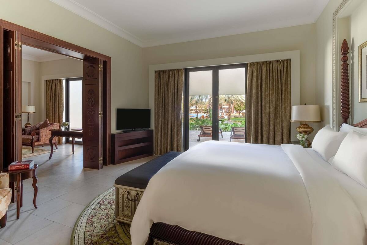 A hotel room with a large bed, a television, a desk, and a view of the outdoor area.