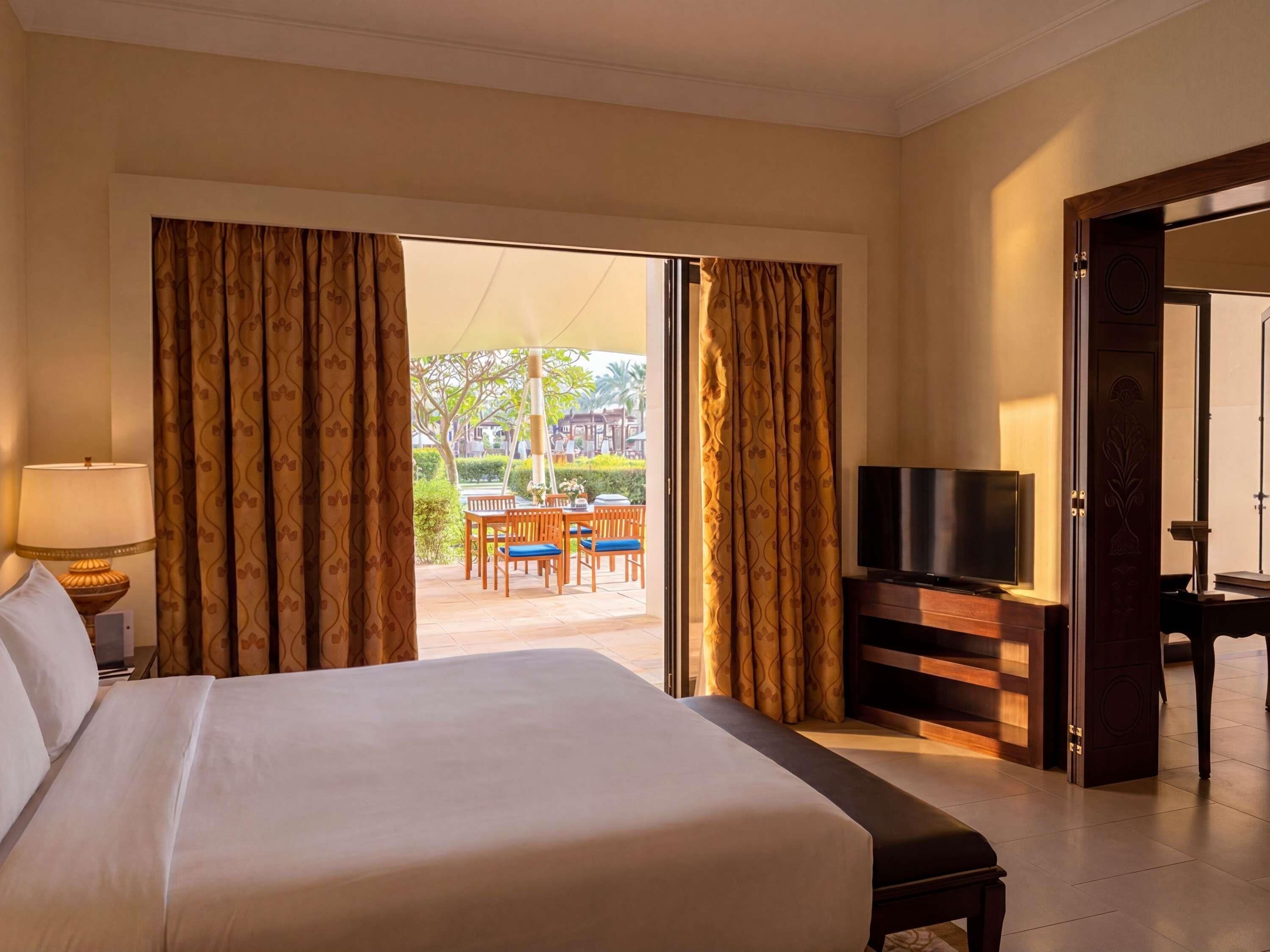 Una habitación de hotel con una cama grande, televisión y vistas a un patio exterior con mesa y sillas.