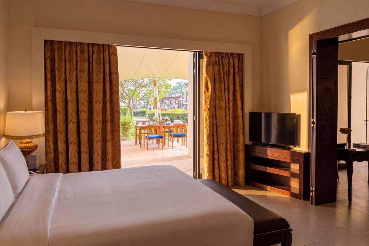 A hotel room with a large bed, a television, and a view of an outdoor patio with a table and chairs.