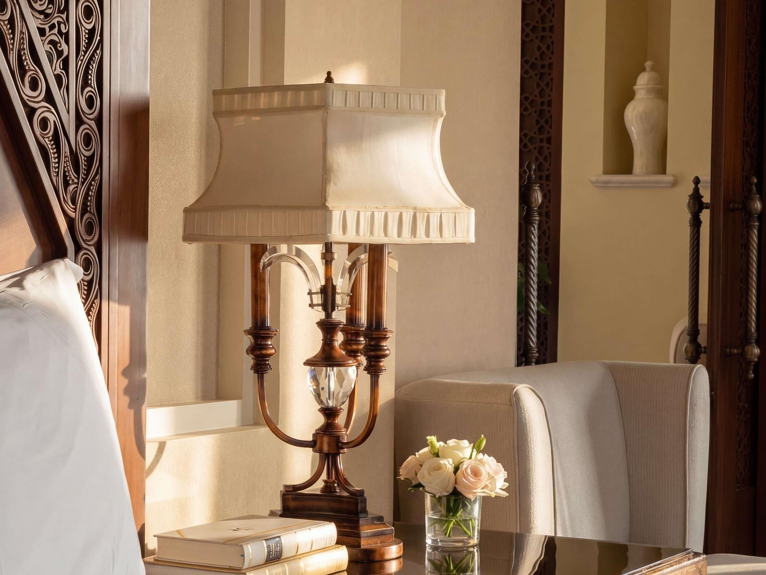 A room with a table, a lamp, a vase with flowers, and a chair.