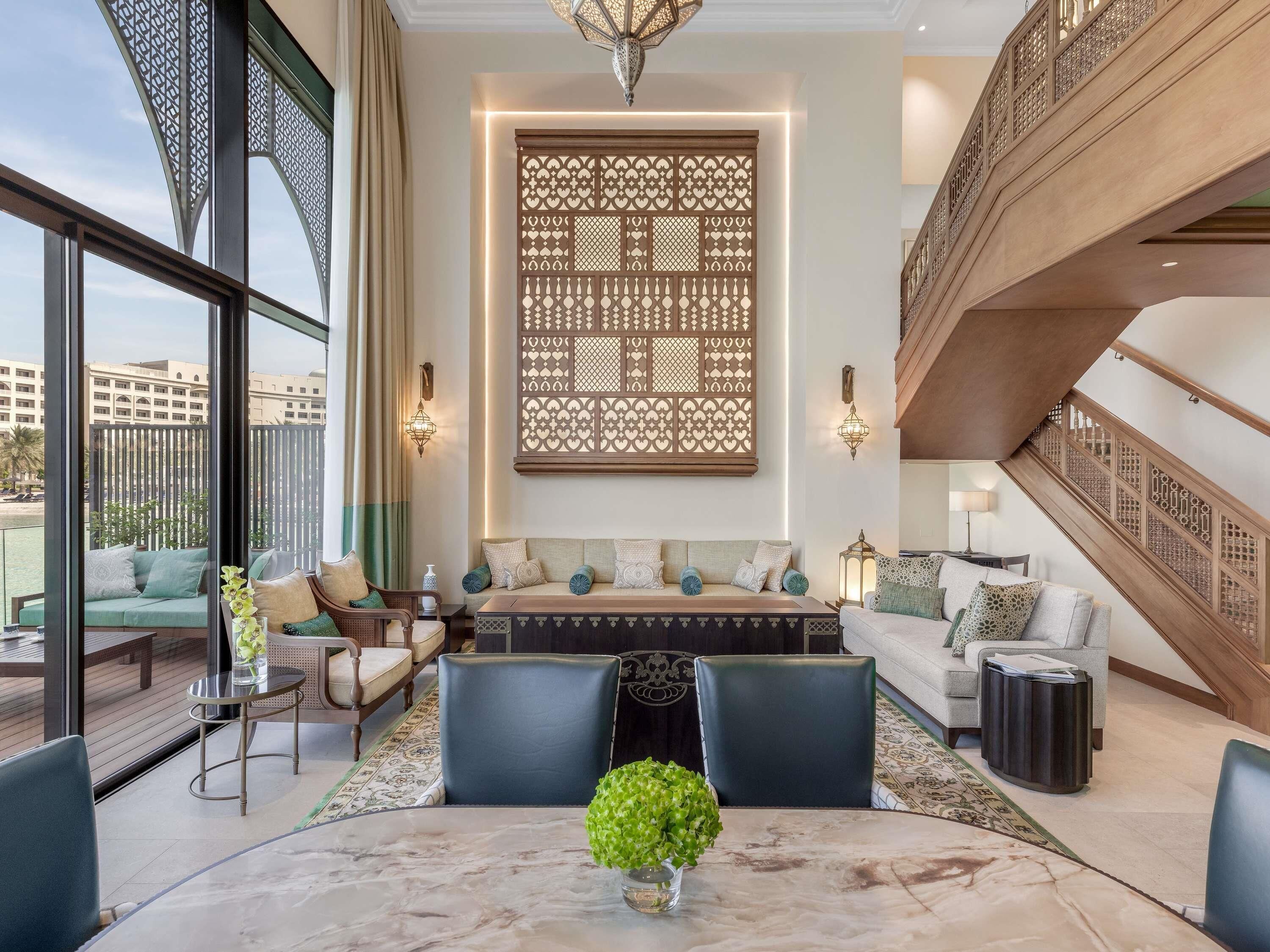 A modern living room with a sofa set, a dining table with a vase of green plants, and a view of the outside.