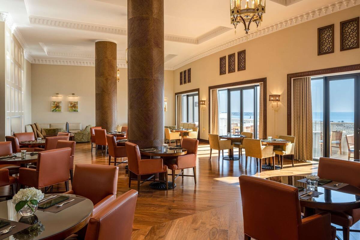 A spacious hotel lobby with high ceilings, large pillars, and a view of the sea through expansive windows.