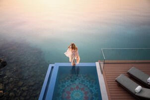 Una persona de pie al borde de una piscina infinita, con vista clara al agua.