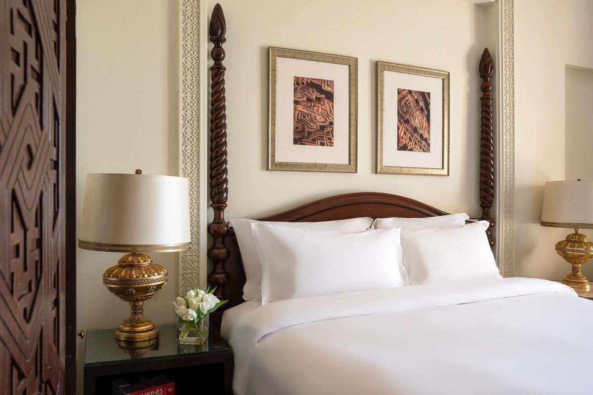 A hotel room with a neatly made bed, two framed pictures on the wall, and a nightstand with a lamp and a vase of flowers.