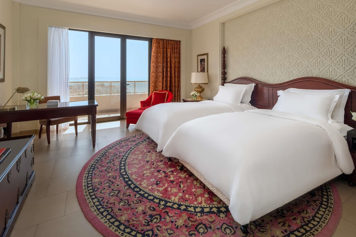 A hotel room with a large bed, a desk, a chair, a balcony with a view, and a patterned wall.