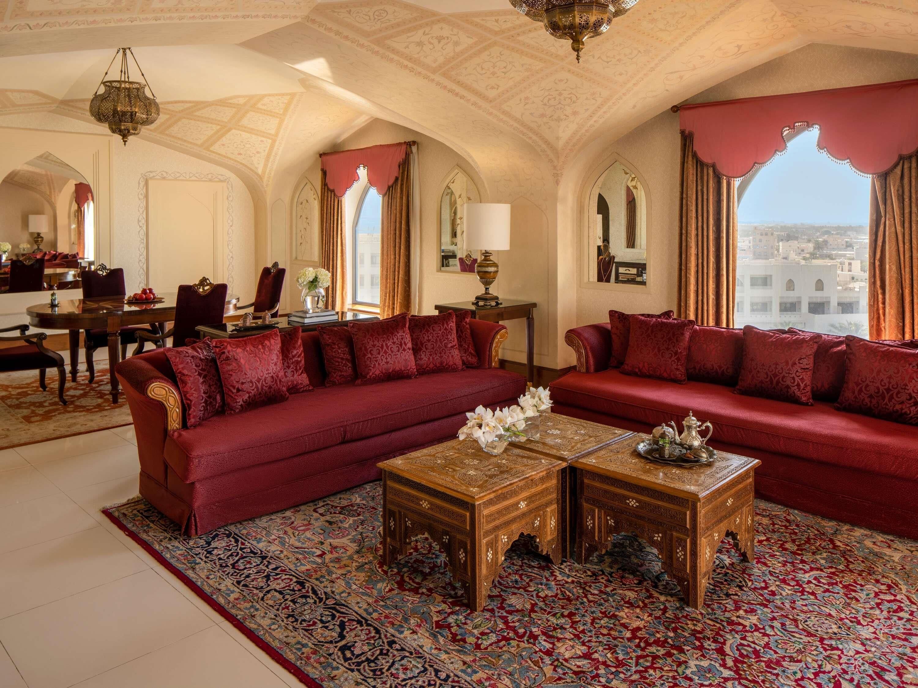 A luxurious room with a red sofa set, ornate wooden coffee table, and a patterned carpet.