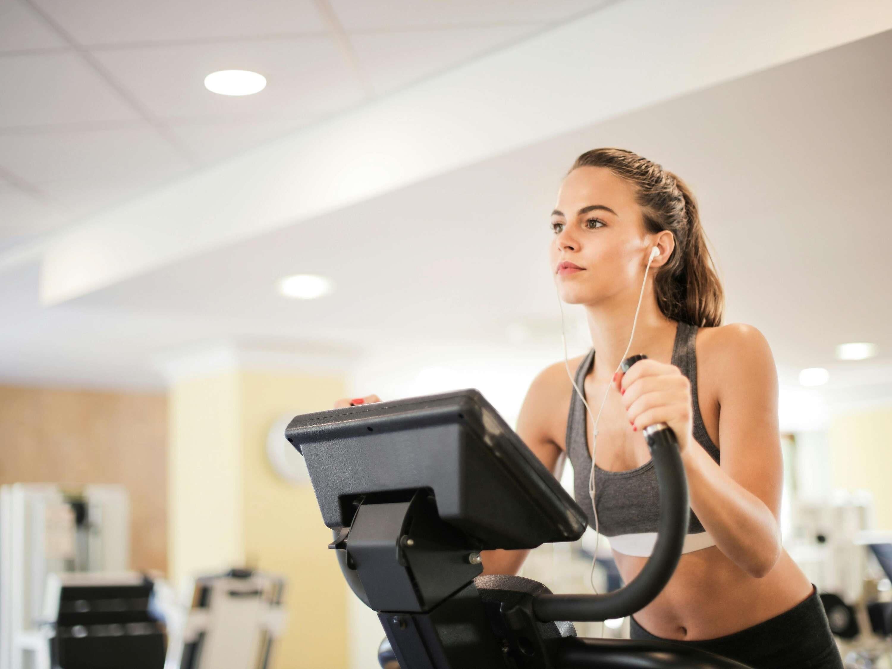 A person using a stationary bike in a gym with various exercise machines in the background.