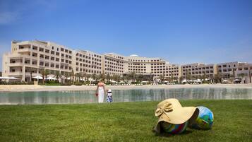 A hotel with multiple floors, a pool, and a grassy area with a hat and a ball.