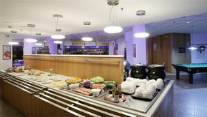 Espaço de buffet com diversos alimentos e uma mesa de bilhar ao fundo.