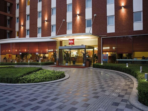 A hotel entrance with a red sign, a glass facade, and a paved walkway. - ibis Chengdu Yongfeng Hotel (Chengdu)
