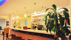 Um hall de hotel com balcão de recepção, cadeiras, uma grande planta em vaso e um painel de azulejos.