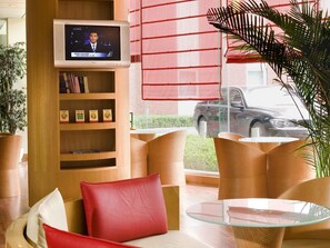 A modern hotel lobby with a flat-screen TV, wooden shelves with books, a glass table, and comfortable seating. - ibis Chengdu Yongfeng Hotel (Chengdu)