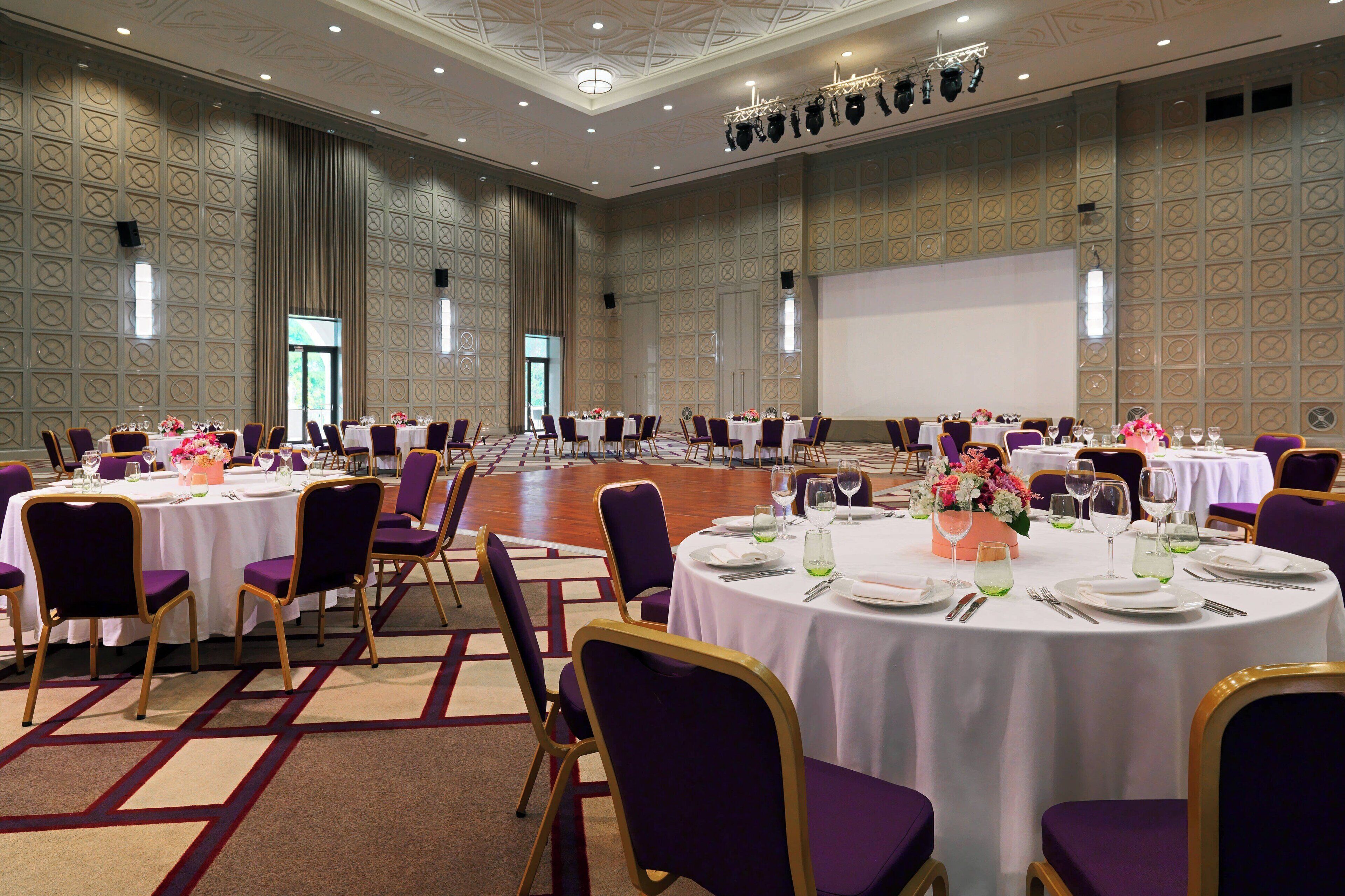 A large conference room with round tables, purple chairs, and white tablecloths.