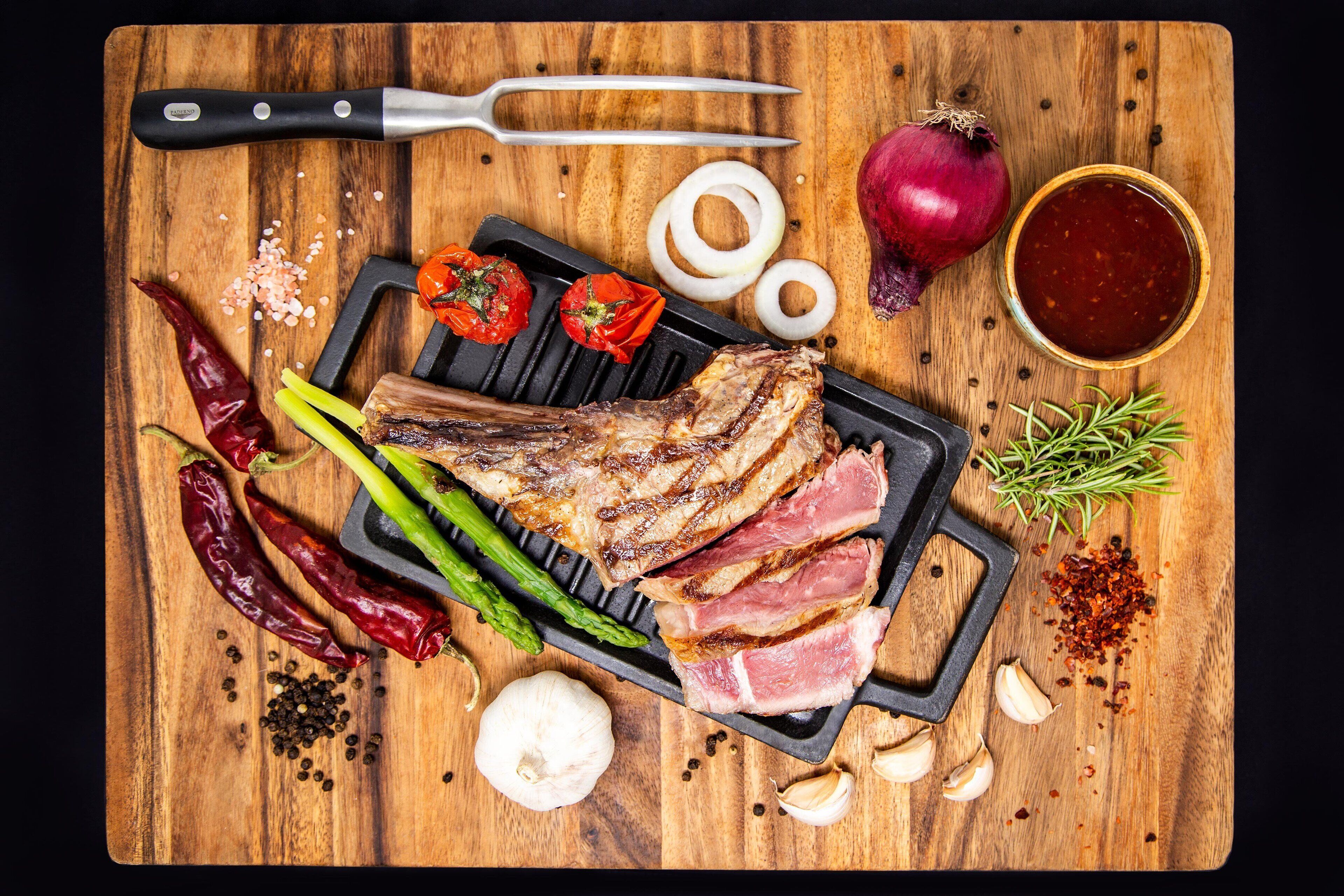Una tabla de madera con carne a la parrilla, verduras y condimentos.
