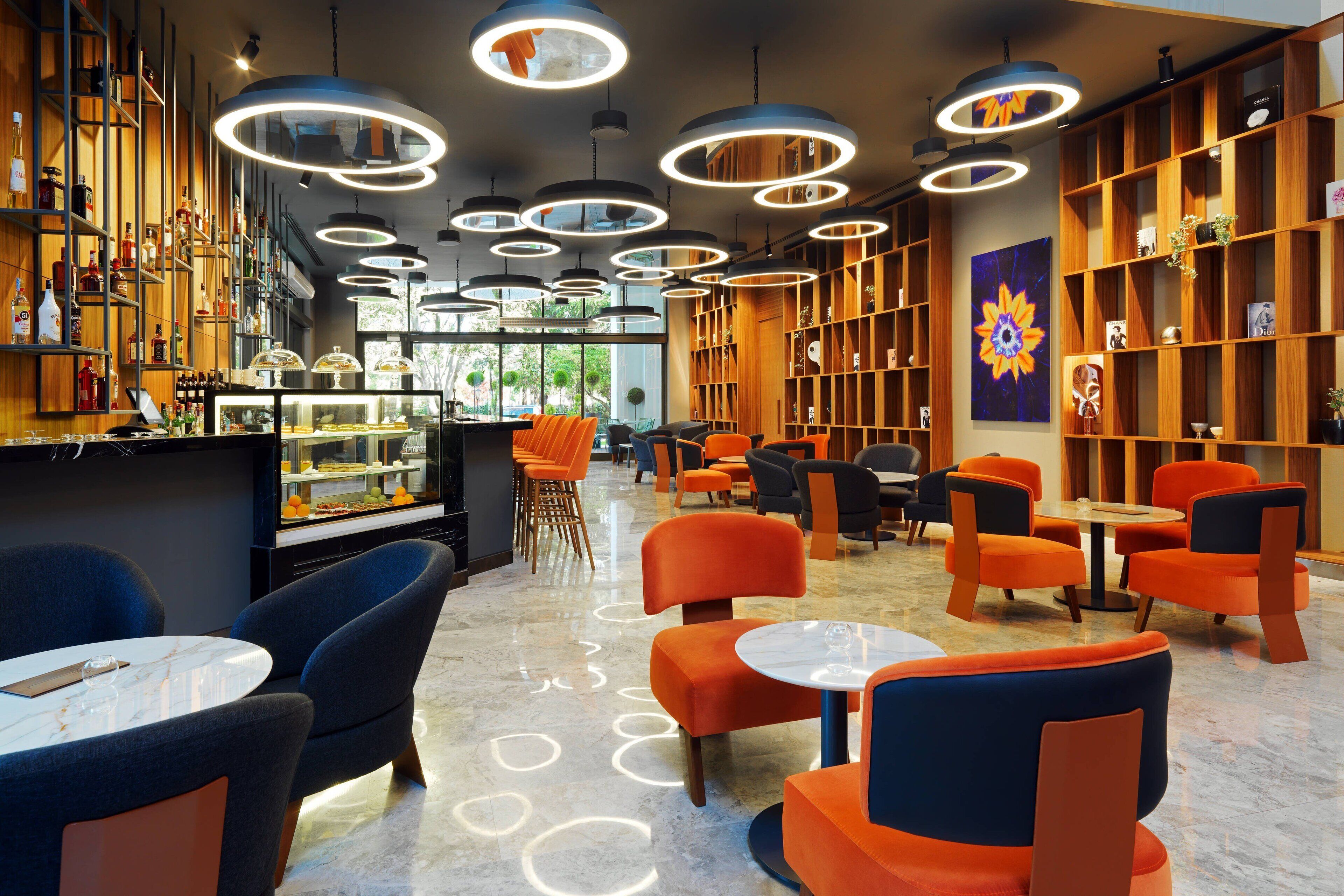 A modern interior with circular ceiling lights, orange and blue seating, and a bar area with shelves of bottles.