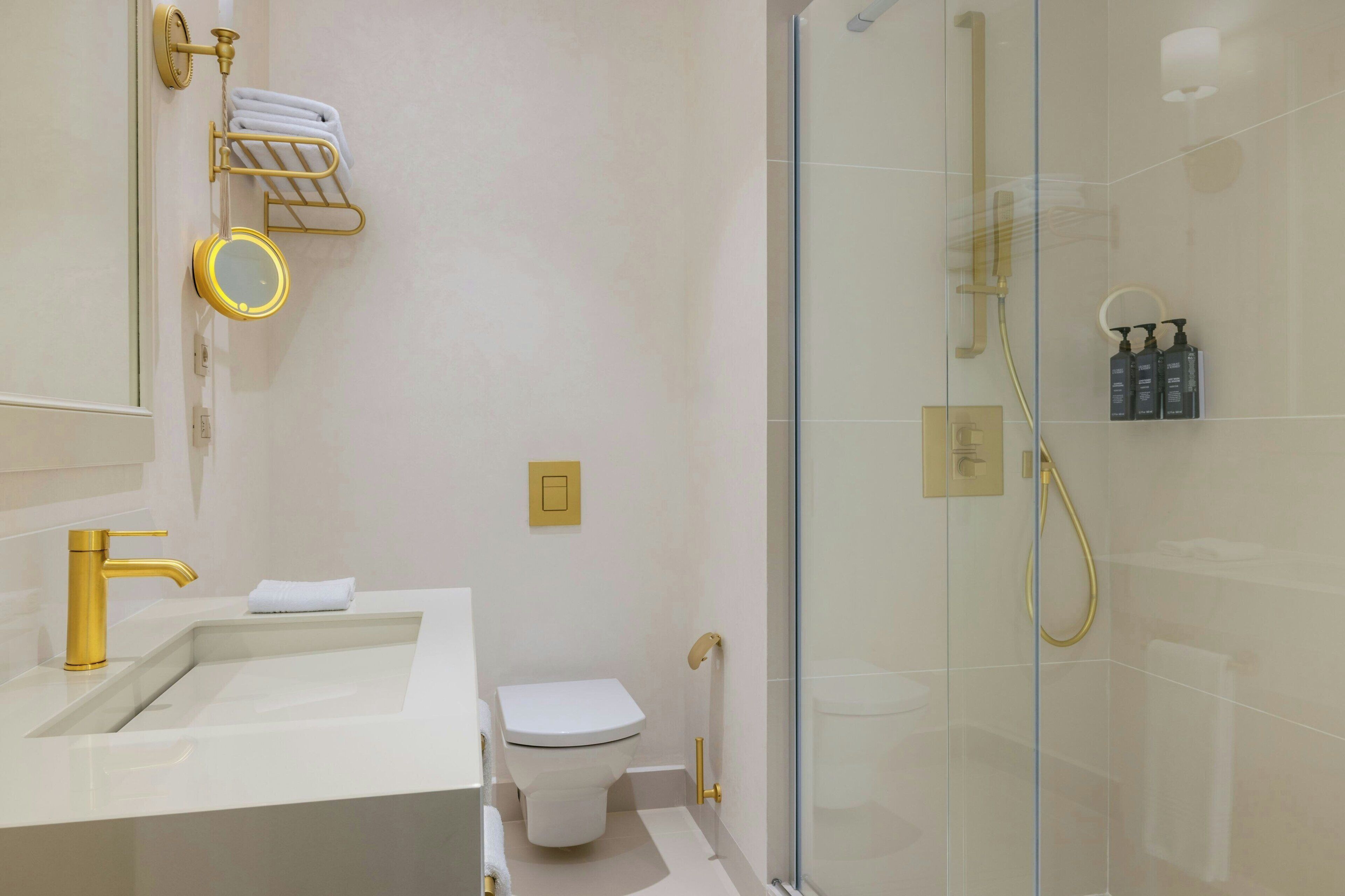 Un bagno moderno con un rubinetto dorato, un lavandino bianco, un water e uno spazio doccia con pareti in vetro.