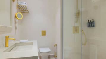 Un baño moderno con grifo dorado, lavamanos blanco, inodoro y cabina de ducha con paredes de vidrio.
