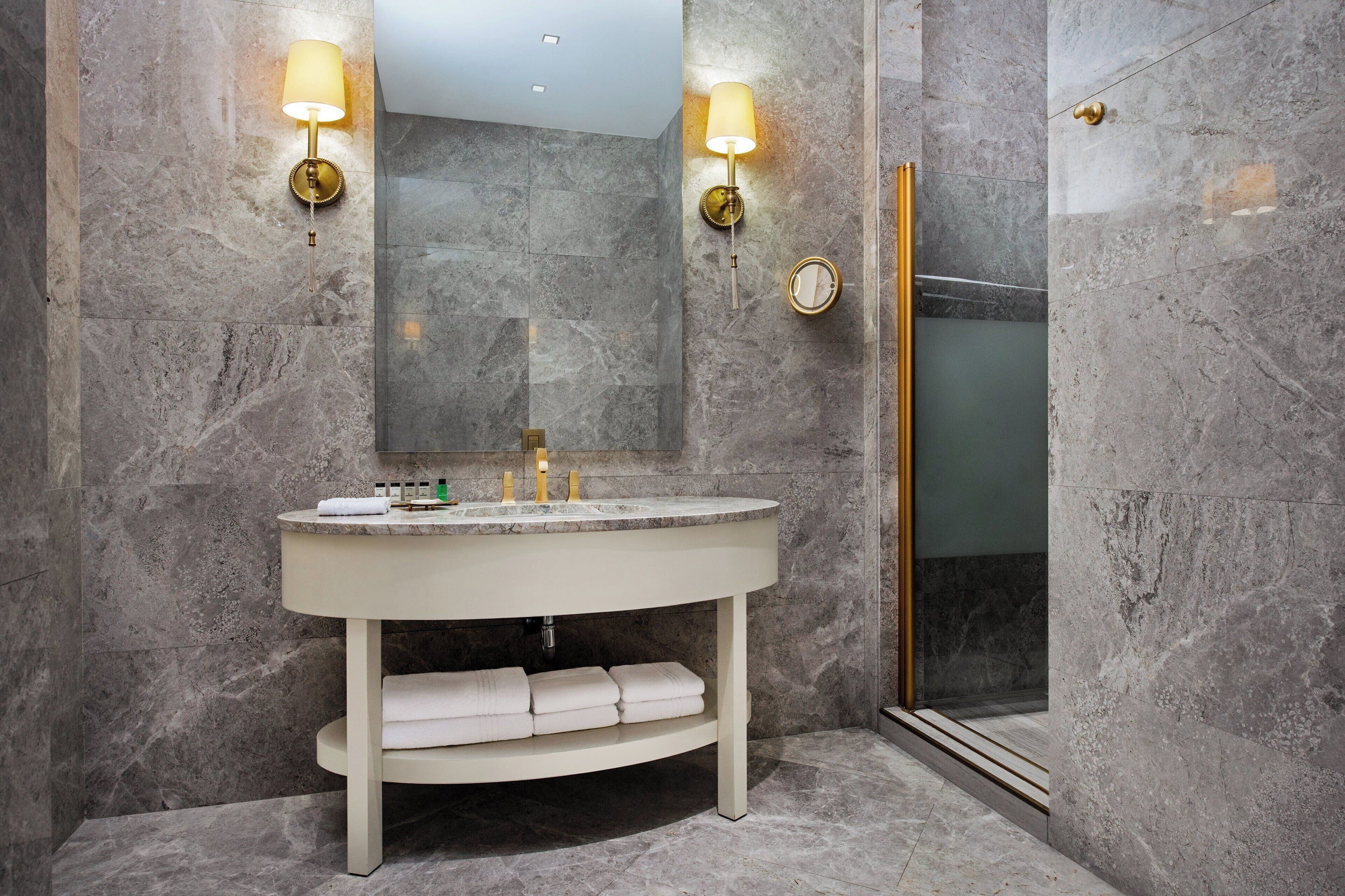 A modern bathroom with a marble sink, two wall-mounted lights, a mirror, and a glass-enclosed shower.