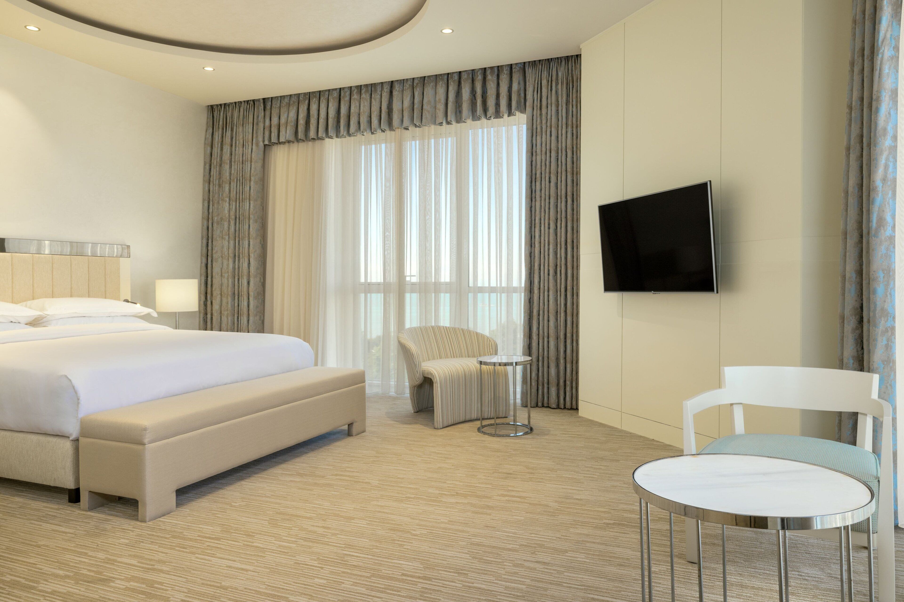 Una habitación de hotel con una cama grande, un televisor montado en la pared, una mesita redonda y una silla.