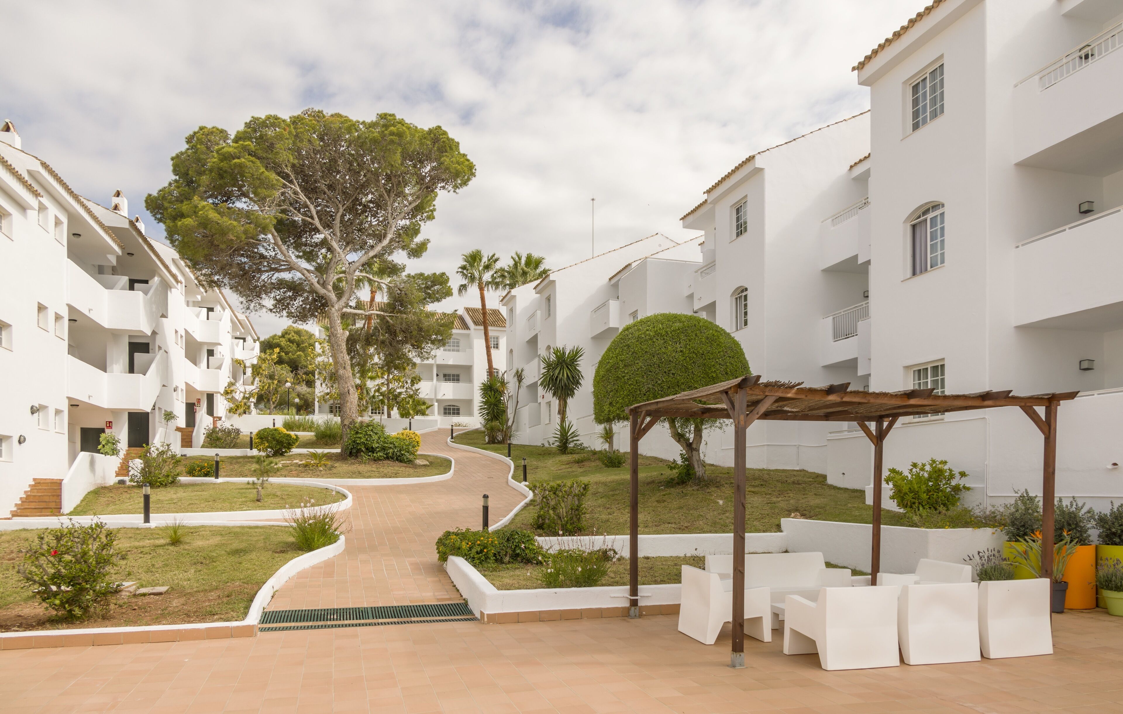 A modern residential building with a central pathway, surrounded by greenery and outdoor seating areas.