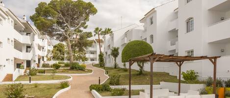 A modern residential building with a central pathway, surrounded by greenery and outdoor seating areas.