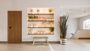 Een modern interieur met een houten deur, een bank, een wandplank met decoratieve objecten en een hoge plant.