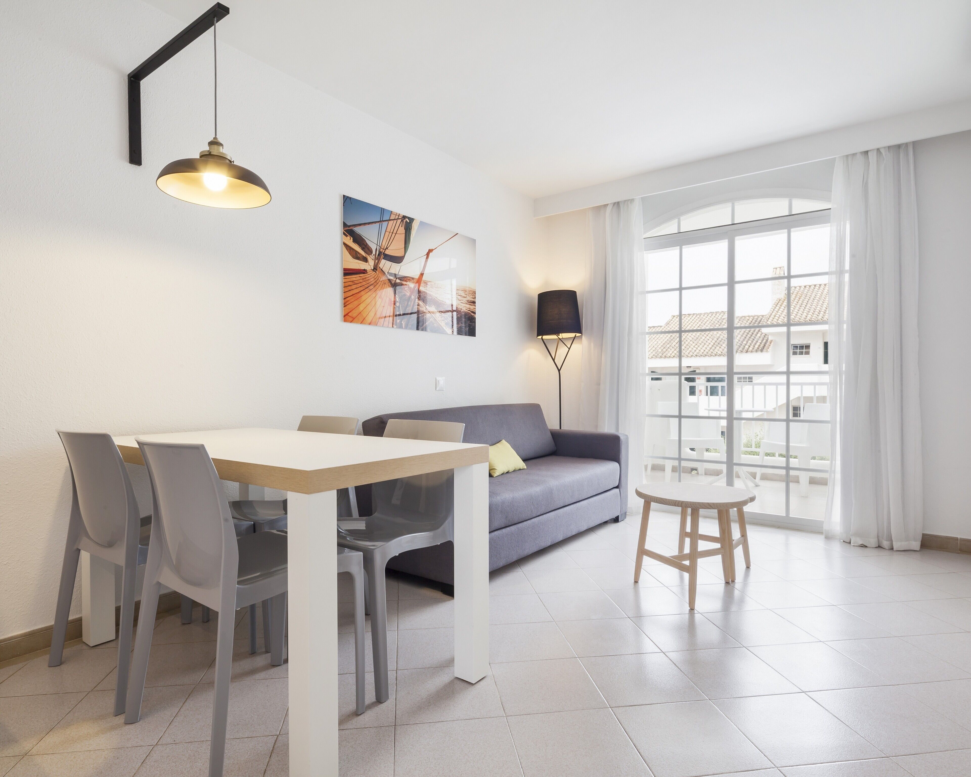Una sala de estar moderna con una mesa de comedor, un sofá gris y un ventanal con cortinas.