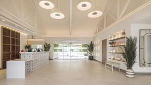 Een ruime lobby met een receptiebalie, moderne hanglampen en een uitzicht op buiten door grote glazen deuren.