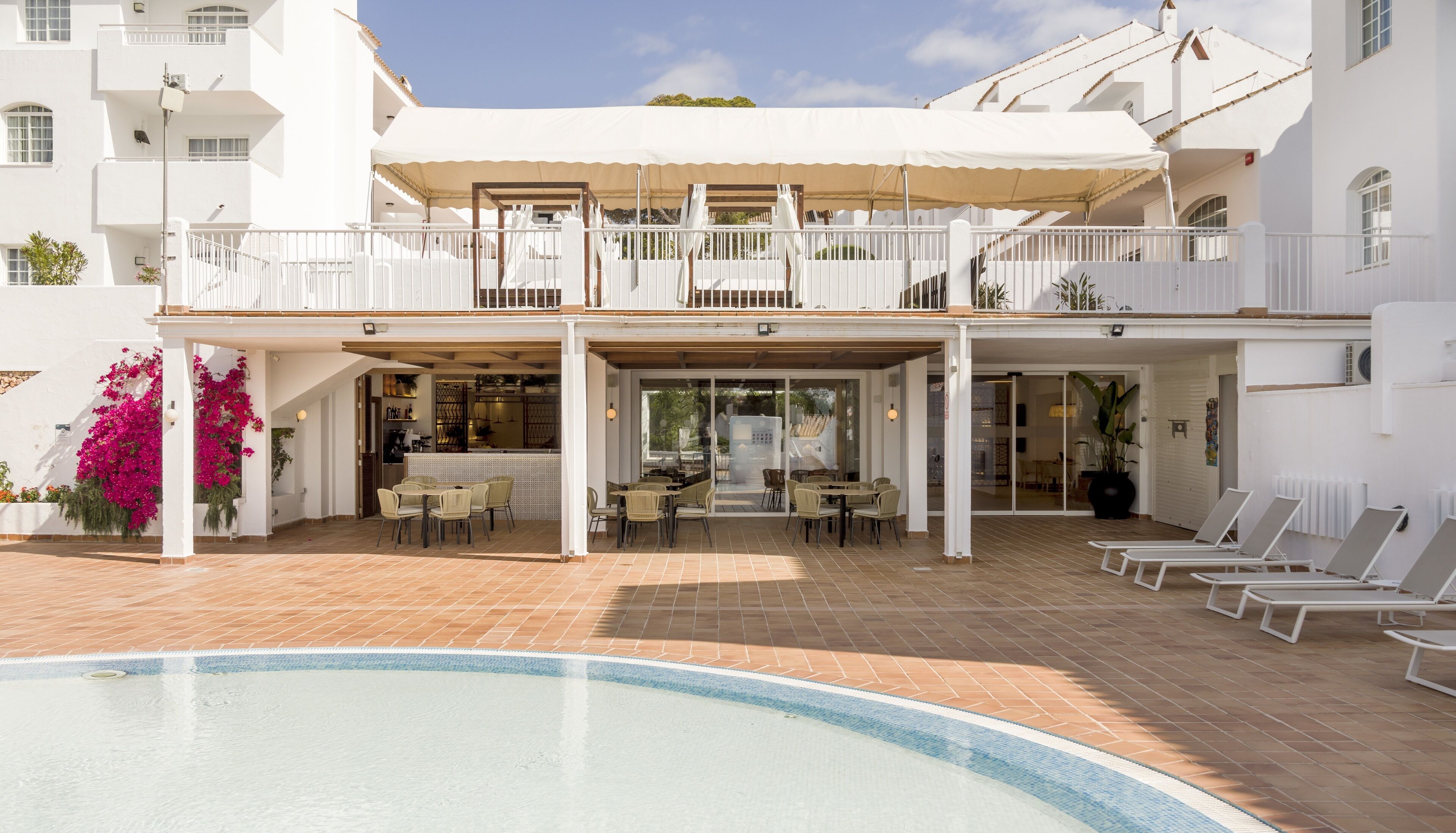 Un espace aménagé au bord de la piscine, comprenant un coin salon couvert, un bar extérieur et des chaises longues.