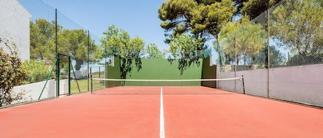 A tennis court with a net, surrounded by green fencing and trees.