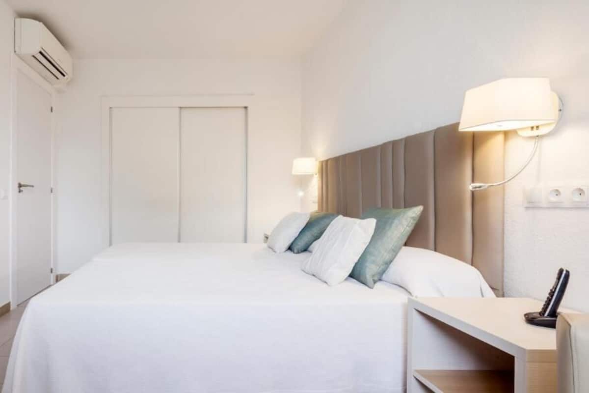 Een hotelkamer met een bed, nachtkastje, lamp en airconditioning.