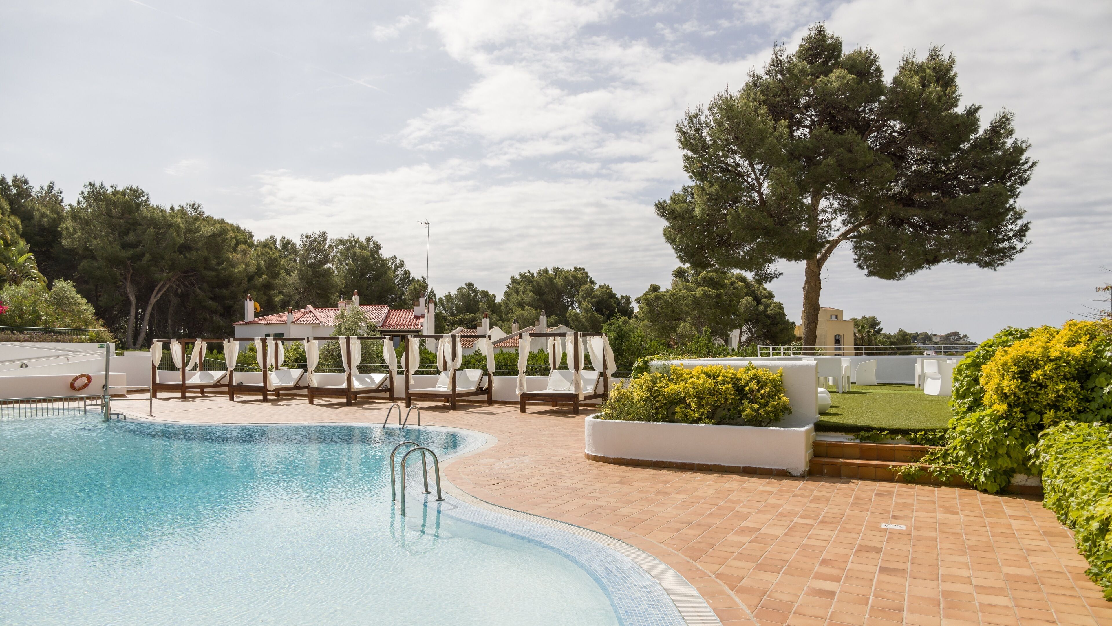 A pool area with a clear pool, sun loungers, and a pergola with white canopies.