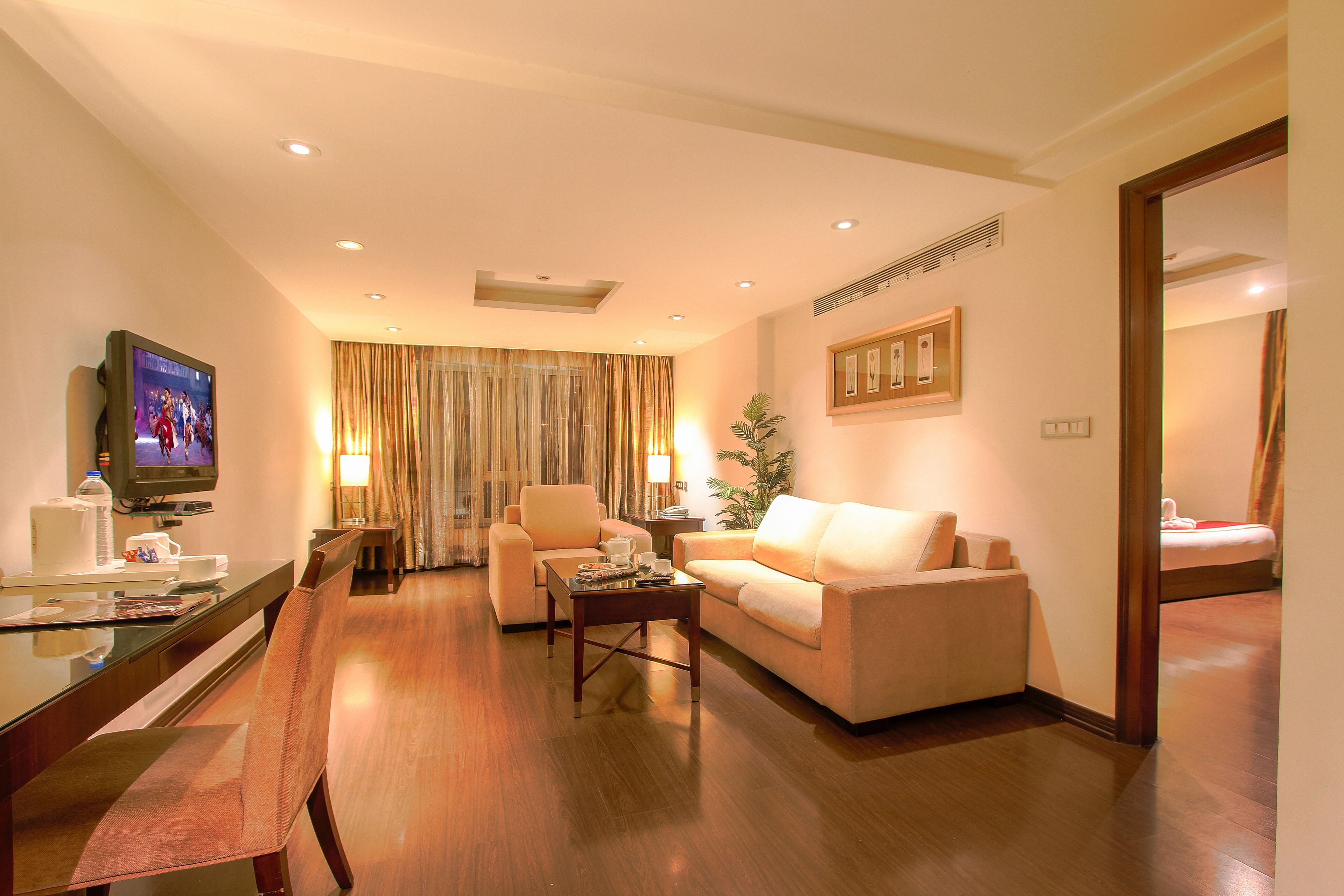A hotel room with a living area featuring a sofa, a coffee table, a TV, and a dining table with chairs.
